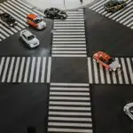 Aerial view of a busy Japanese intersection with multiple cars, including taxis, moving in different directions across a crosswalk.
