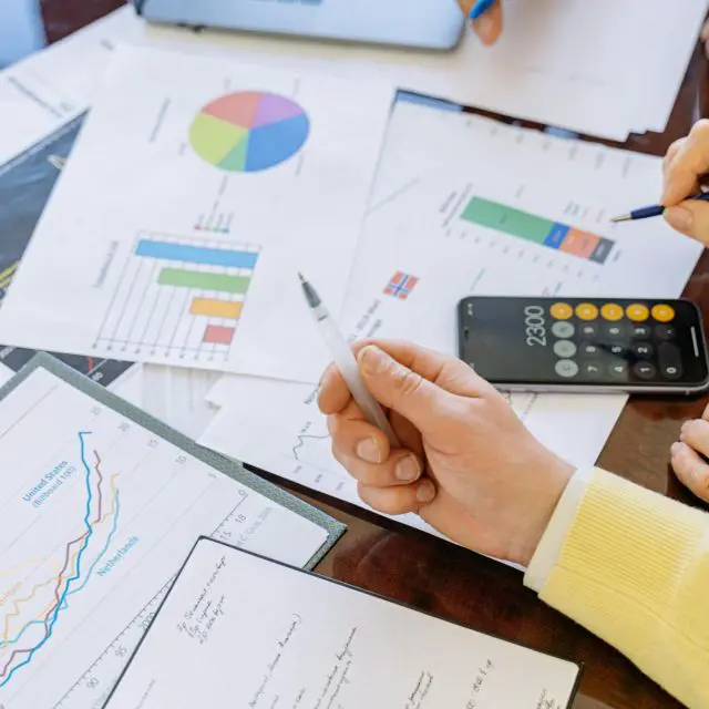 A person in a yellow shirt holding a pen over pages with graphs on a desk.
