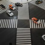 Aerial view of a busy Japanese intersection with multiple cars, including taxis, moving in different directions across a crosswalk.